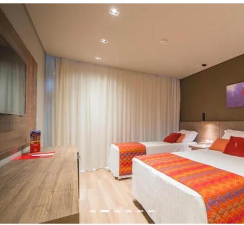 a hotel room with two beds and a television at Quarto no Hotel Laghetto Stillo da Borges in Gramado