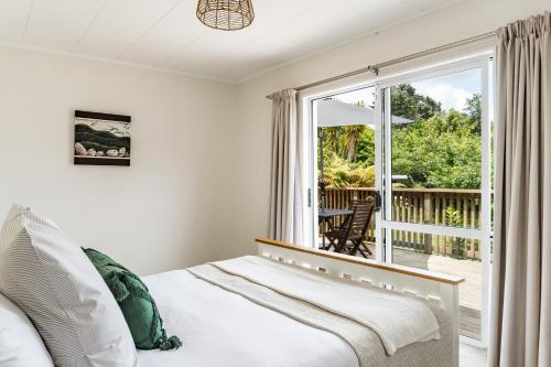 a bedroom with a bed and a sliding glass door at Calypso Cottage, Bright bach, Water view in Raglan