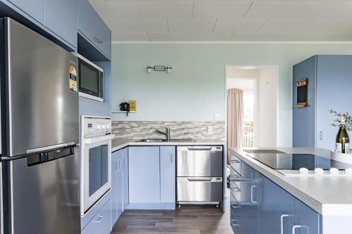 a kitchen with blue cabinets and a stainless steel refrigerator at Calypso Cottage, Bright bach, Water view in Raglan