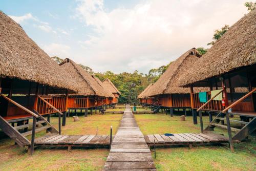 eine Reihe von Hütten mit Strohdächern und einem Holzweg in der Unterkunft Waita Lodge in Cuyabeno