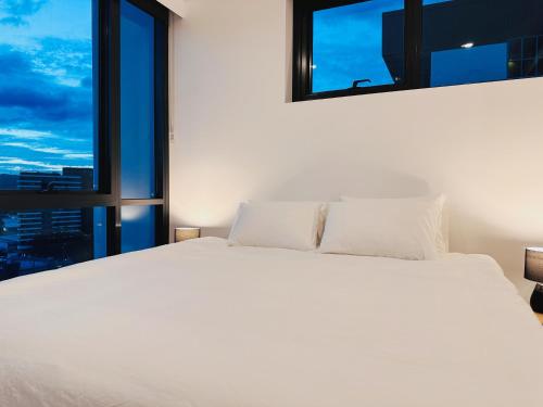 a bedroom with a large white bed with windows at Art House with 2 Kingbeds at Cultural Centre in Brisbane