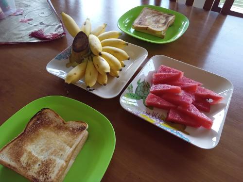 a table with plates of fruit and toast and a bunch of bananas at Dannu's Homestay Ijen and Bromo Tour in Banyuwangi