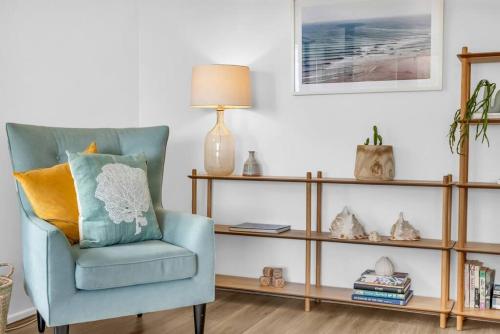 a living room with a blue chair and a book shelf at Seaglass at Pambula Beach in Pambula Beach