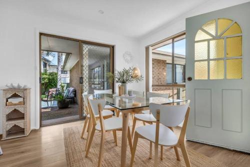 a dining room with a glass table and white chairs at Seaglass at Pambula Beach in Pambula Beach