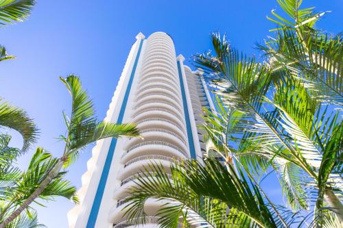 a tall building with palm trees in front of it at Aegean Resort Apartments in Gold Coast