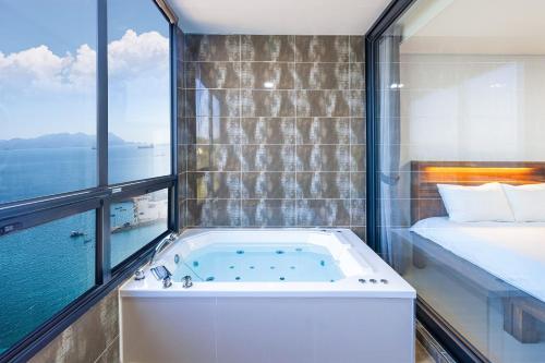 a bath tub in a room with a bed and a window at Le Paradis Ocen view Spa Pension in Yeosu