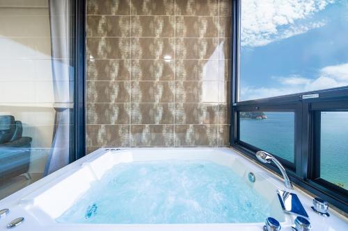 a bath tub in a room with a large window at Le Paradis Ocen view Spa Pension in Yeosu