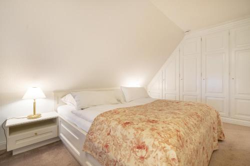 a white bedroom with a bed and a lamp on a night stand at Haus Süderende in Keitum