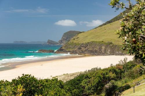 a beach with the ocean and mountains in the background at Barefoot on Blueys in Blueys Beach