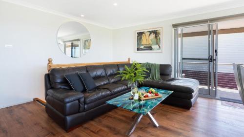 a black leather couch in a living room with a table at Marilyn's in Callala Beach