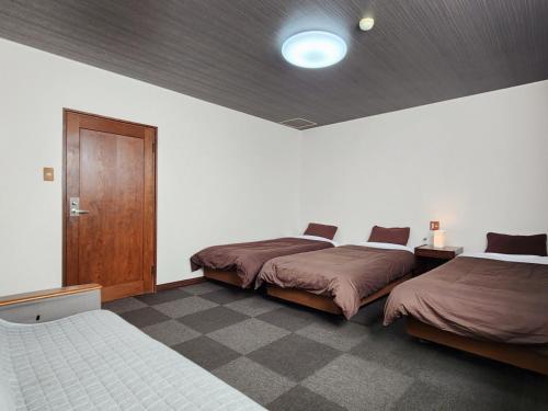 a bedroom with two beds and a wooden door at Pension Kobekko in Otari