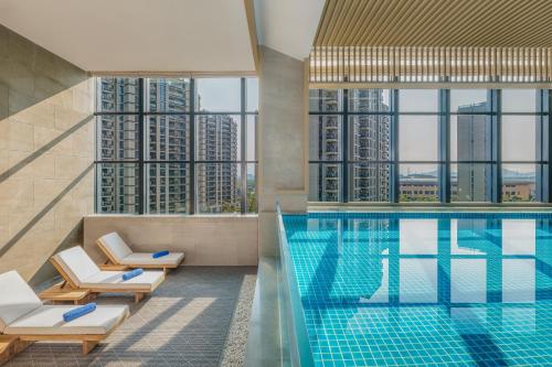 einen Hotelpool mit Stühlen und Blick auf Wolkenkratzer in der Unterkunft Shaoxing Marriott Hotel Shangyu in Shaoxing