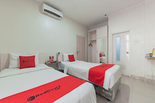 two beds in a white room with red and white sheets at RedDoorz near Pasar Baru Bandung in Bandung