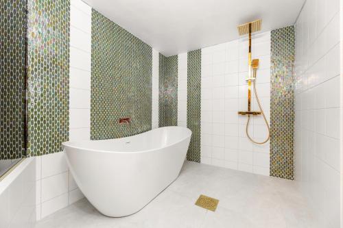 a white tub in a bathroom with green and white tiles at Cozy private house in Nõmme in Tallinn