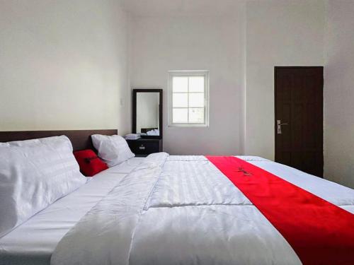 a large white bed with a red stripe on it at RedDoorz near Stasiun Pematangsiantar in Pematangsiantar
