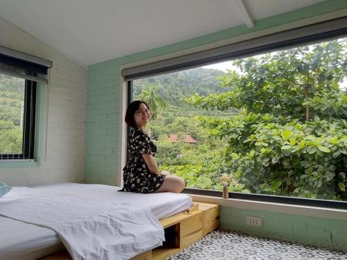 una mujer sentada en una cama mirando por la ventana en Ba Vì Madela, en Ba Vì