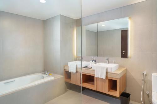 y baño con lavabo, bañera y espejo. en Golden Tulip Springhill Lampung en Bandar Lampung