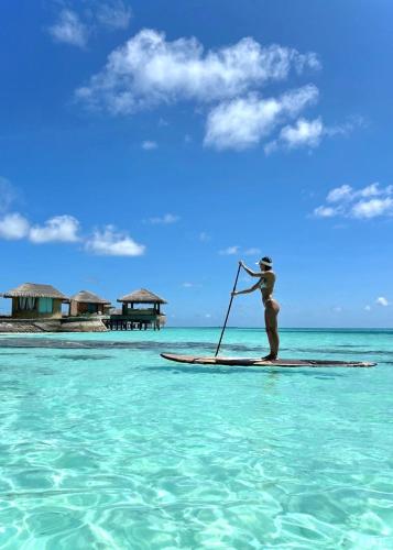 a man standing on a paddle board in the ocean at You & Me Maldives - Adults Only - Premium All-Inclusive in Raa Atoll