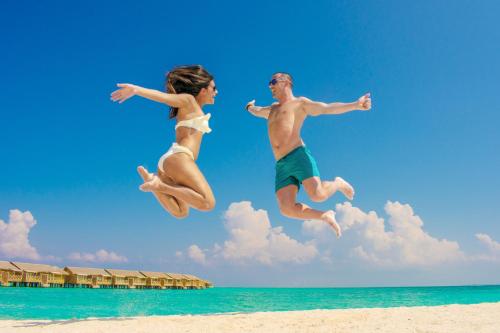 a man and woman jumping in the air on the beach at You & Me Maldives - Adults Only - Premium All-Inclusive in Raa Atoll