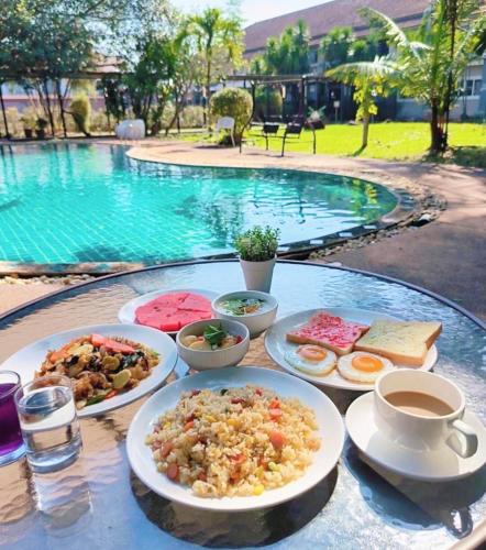 a table with plates of food on a table near a pool at The Space Airport Hotel Chiang Rai in Ban Du