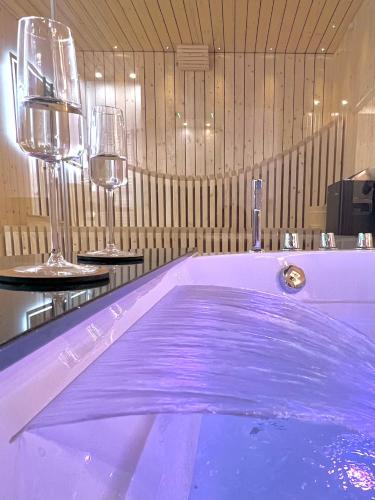 a tub with purple water in a room with wine glasses at Le Zen - Sauna - Balnéo - Sparoom Sarreguemines in Sarreguemines