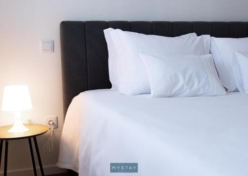 a bed with white pillows and a lamp on a table at MyStay - D Maria Apartments in Vila Nova de Famalicão