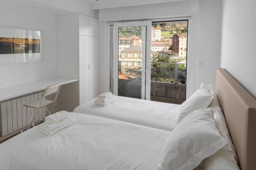 a white bedroom with two beds and a window at Bright apartment with A/C, parking optional in San Sebastián