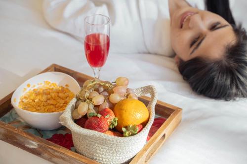 a woman laying in bed with a tray of fruit and a glass of wine at The Namah Retreat By PerfectStayz in Shimla