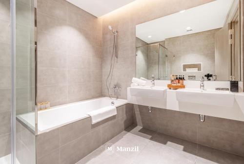 een badkamer met een bad, een wastafel en een spiegel bij Manzil - 3BR + Maid in District One with Burj View in Dubai