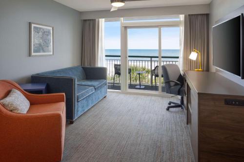 a living room with a couch and a television and a balcony at Hampton Inn & Suites Myrtle Beach Oceanfront in Myrtle Beach