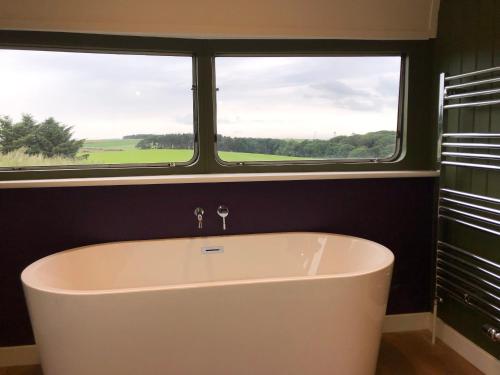 a bath tub in a bathroom with two windows at Middlemoor Farm Holidays in Alnwick