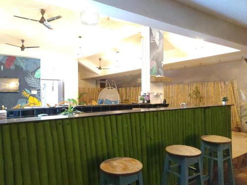 a bar with three stools in front of a green wall at Passions de Goa in Anjuna