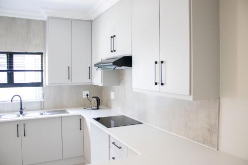 a white kitchen with white cabinets and a sink at Asania Guest House in Bloemfontein