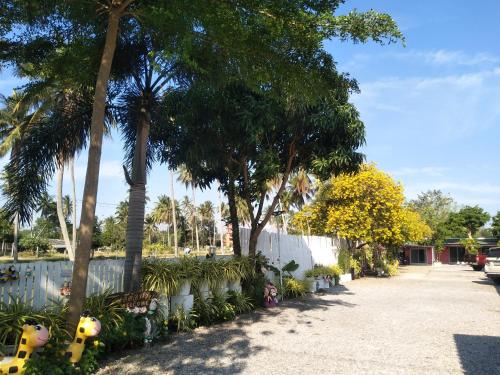 a driveway with palm trees and a white fence at Saan Rak Resort in Prachuap Khiri Khan