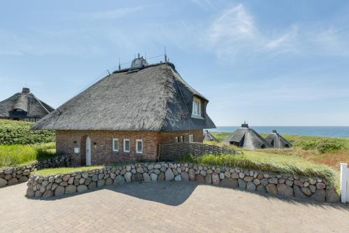 a house with a thatched roof and a stone wall at Smuk Hus in Hörnum