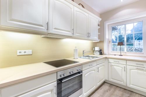 a kitchen with white cabinets and a sink and a window at Wattlaeufer in Keitum