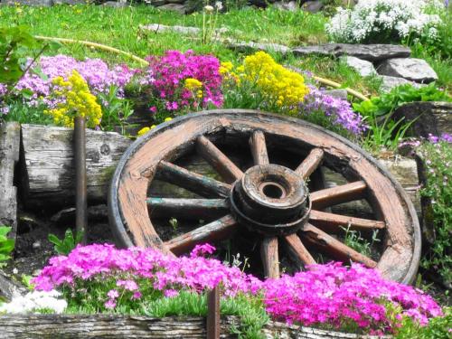 a wooden wheel in a garden with flowers at Rooms Alpe Veglia-Varzo in Varzo