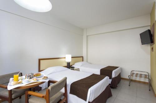 a hotel room with two beds and a table and chairs at Black Stream Hotel in Ribeirão Preto