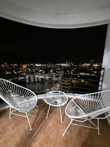 three white chairs on a balcony with a view of a city at Departamento Boulevard con cochera in Santa Fe