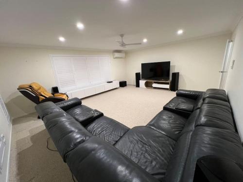 a living room with a leather couch and a flat screen tv at Gardens by the Bay - Acreage Living & EV Charging in Deception Bay