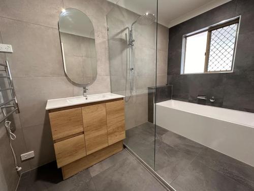 a bathroom with a sink and a tub and a mirror at Gardens by the Bay - Acreage Living & EV Charging in Deception Bay