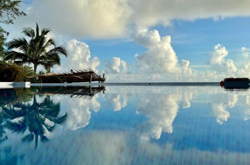 una palmera sentada junto a una piscina con un reflejo del cielo en Marafiki Bungalows en Kiwengwa