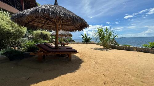 a beach with two lounge chairs under an umbrella at VERONIKA Resort Nosy Komba in Nosy Komba