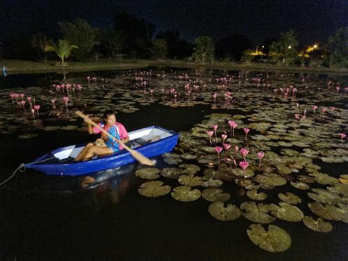 a boy is rowing a boat in a pond with flowers at Bua Daeng Homestay Resort in Amphoe Kumphawapi