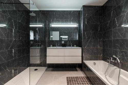 La salle de bains est pourvue de carrelage noir, d'un lavabo et d'une baignoire. dans l'établissement Villa Riviera - Nouveaute entre mer et montagnes, à Colomars