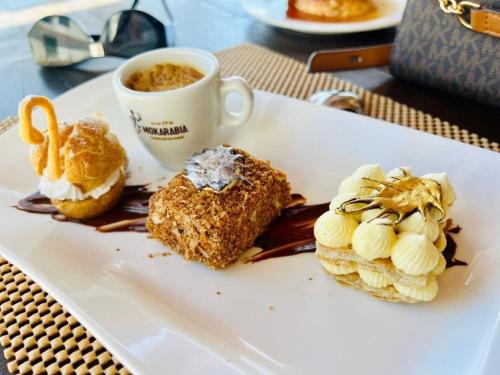 a white plate with desserts and a cup of coffee at Hôtel Grand Bay in Nosy Be