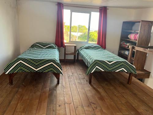 two beds in a room with wooden floors and a window at Hyepy in Punta Del Diablo