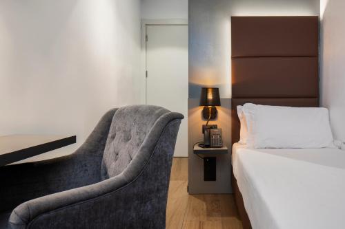 een slaapkamer met een bed en een stoel naast een bed bij London Hotel in Milaan