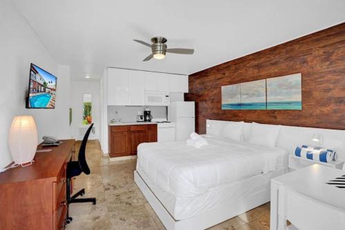 a bedroom with a white bed and a desk and a kitchen at Waves Beach Town Studio Apartment in Pompano Beach