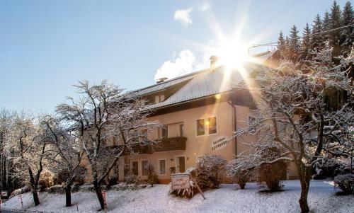 a building in the snow with the sun shining at Gästehaus Seewinkel in Presseggersee